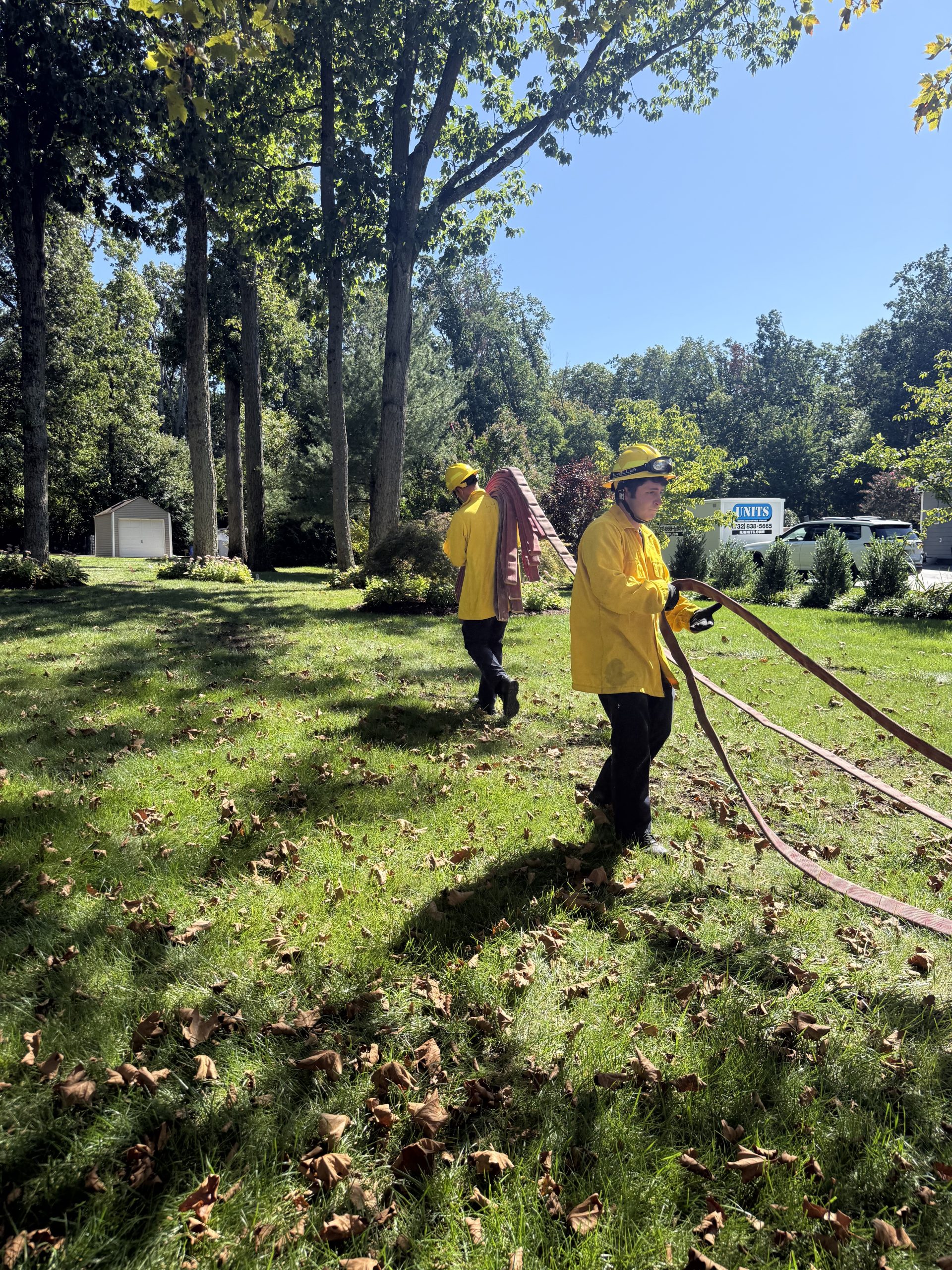 Two firefighters deploy a hose line across a lawn during a training exercise.