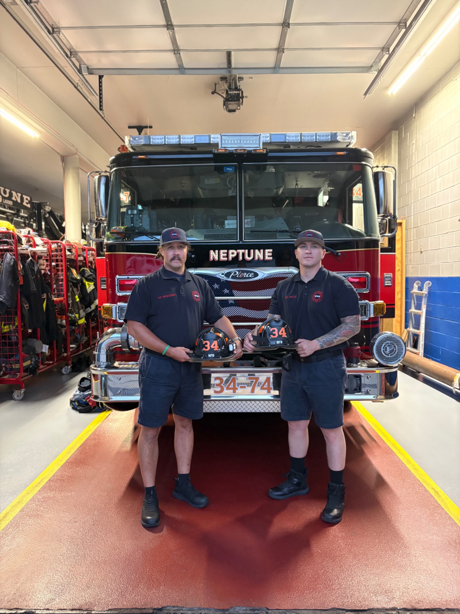 Firefighters David Hoecker and John Fritz Jr. holding their helmets in front of a Neptune fire engine.